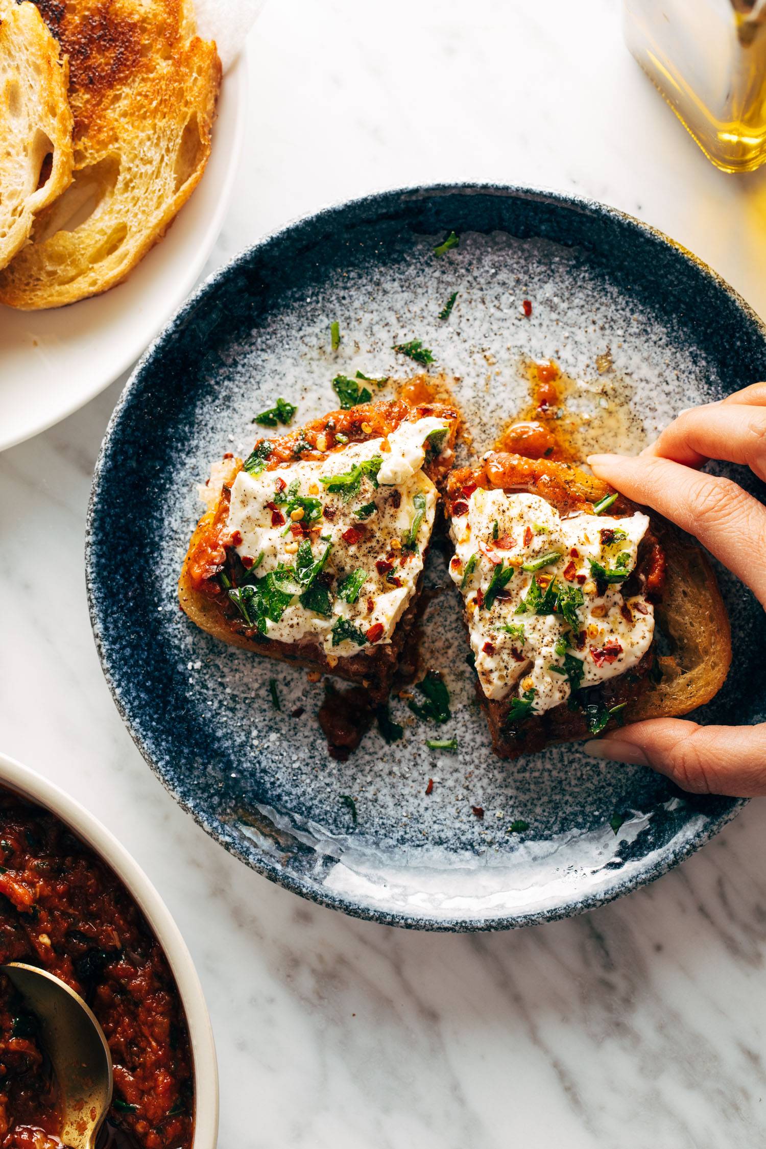 White hand grabbing Zaalouk toast on a plate