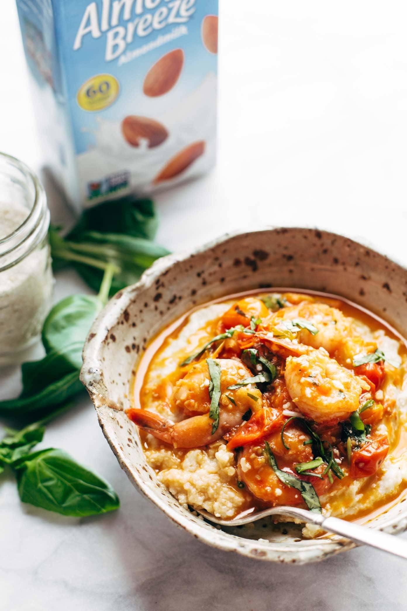 Shrimp and grits in a bowl with a fork and almond breeze almond milk in the background.